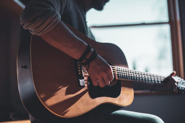 Mężczyzna grający na gitarze akustycznej przed oknem.