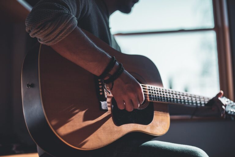 Mężczyzna grający na gitarze akustycznej przed oknem.