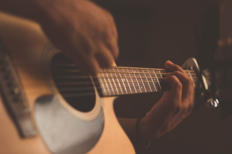 Zbliżenie osoby grającej na gitarze akustycznej ukazujące kunszt i umiejętności najlepszych polskich gitarzystów XXI wieku.